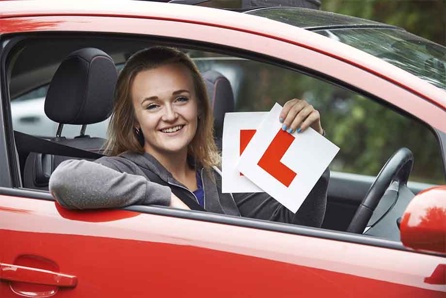 Learner driver holding up her L-plates, an essential item if you want to learn to drive